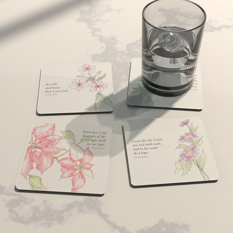 Four watercolor Psalm coasters on white marble with a glass of ice water: pink blooms, purple asters, pink phlox and bluebonnets