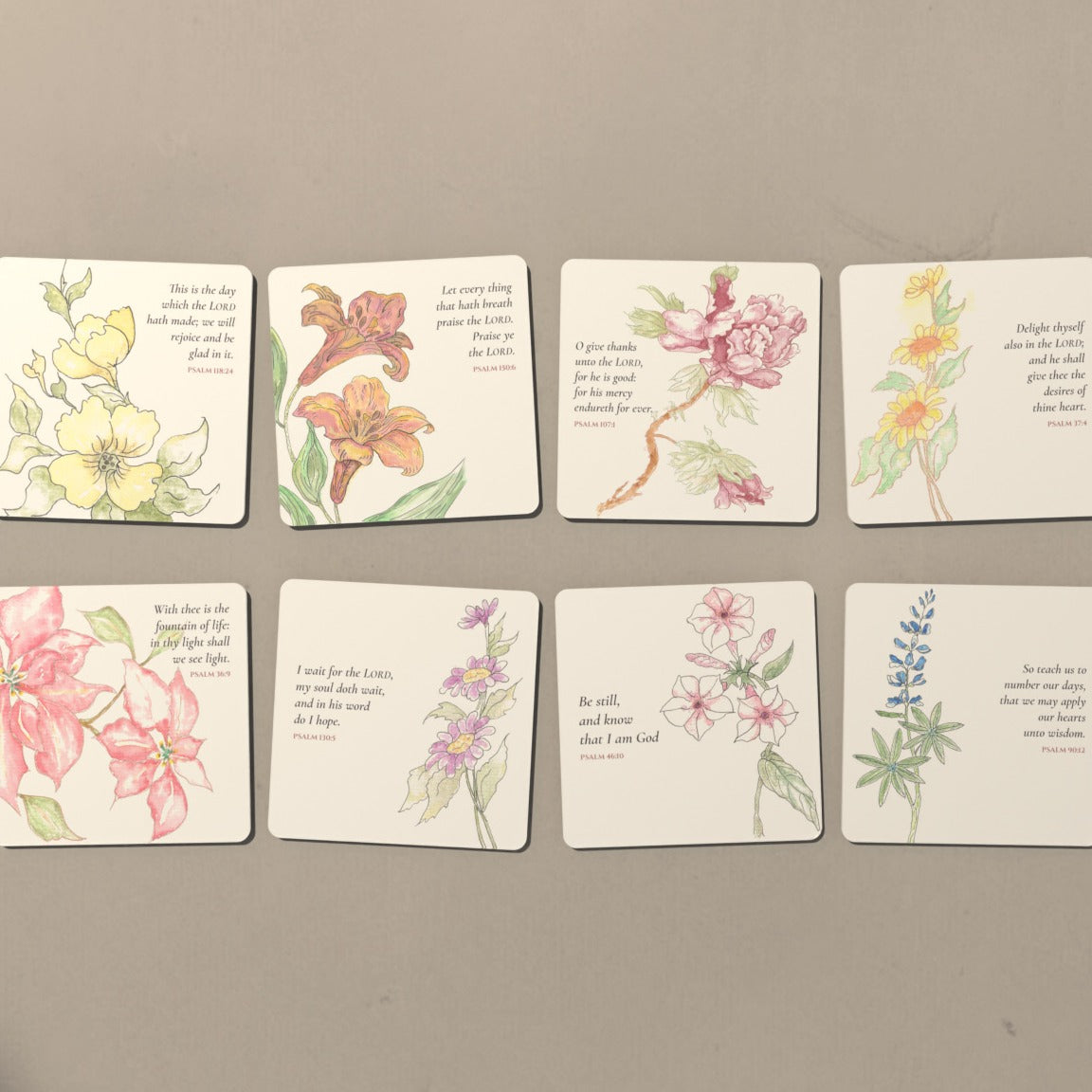 All eight watercolor Psalm coasters laid out in two rows on a warm plaster table